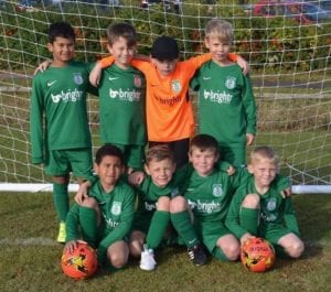 A children's football team in green and orange branded kits posing by a goal with footballs