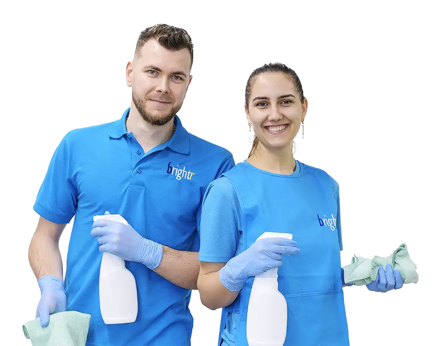 Two cleaners in branded polo shirts holding spray bottles and cloths, smiling