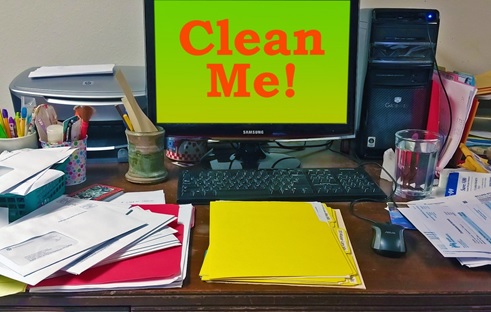 A cluttered desk with a computer monitor showing the message "clean me!"