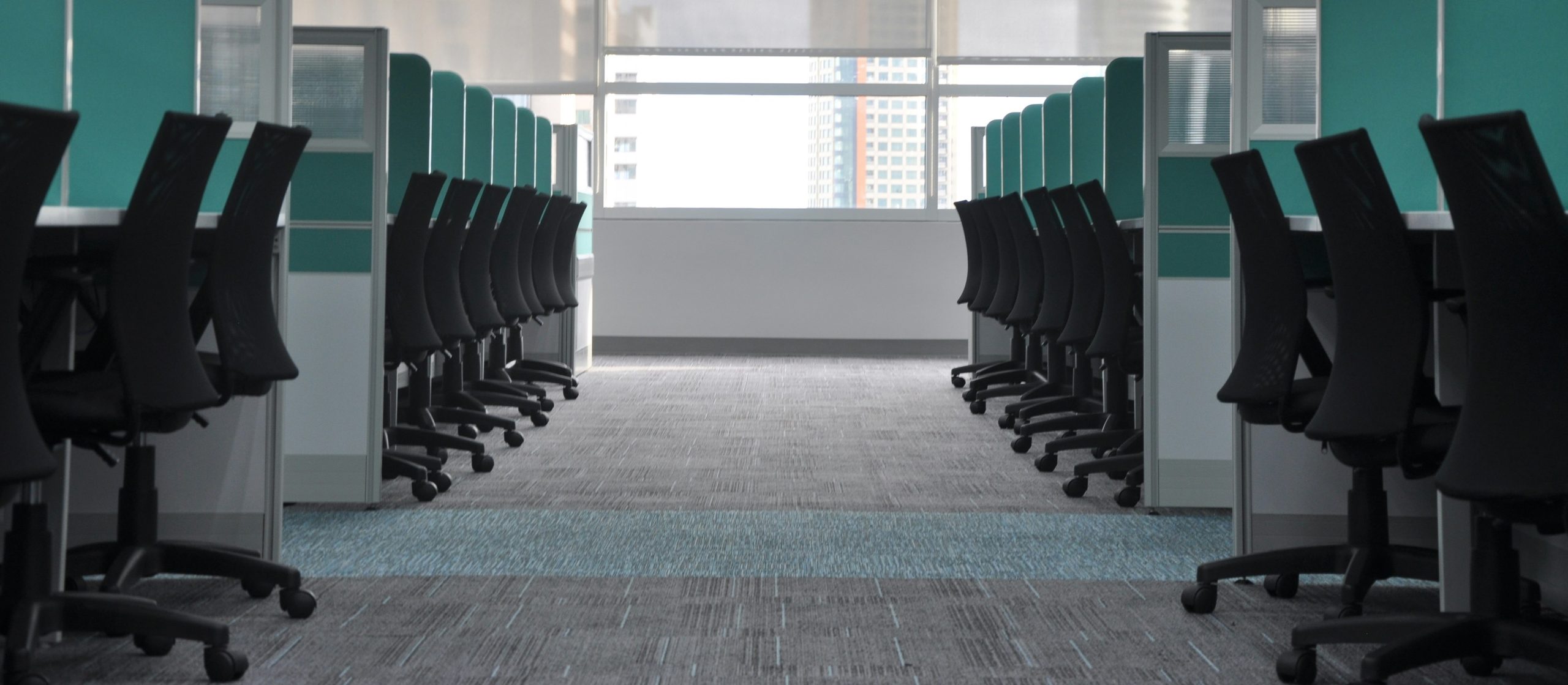 Rows of empty office chairs at desks in an open-plan office with a city skyline view