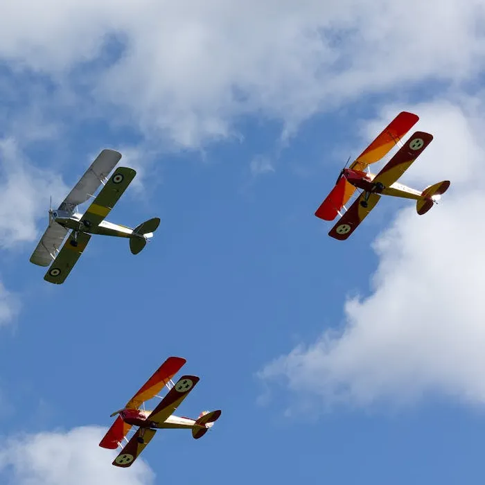 Three vintage biplanes flying in formation against a blue sky with clouds