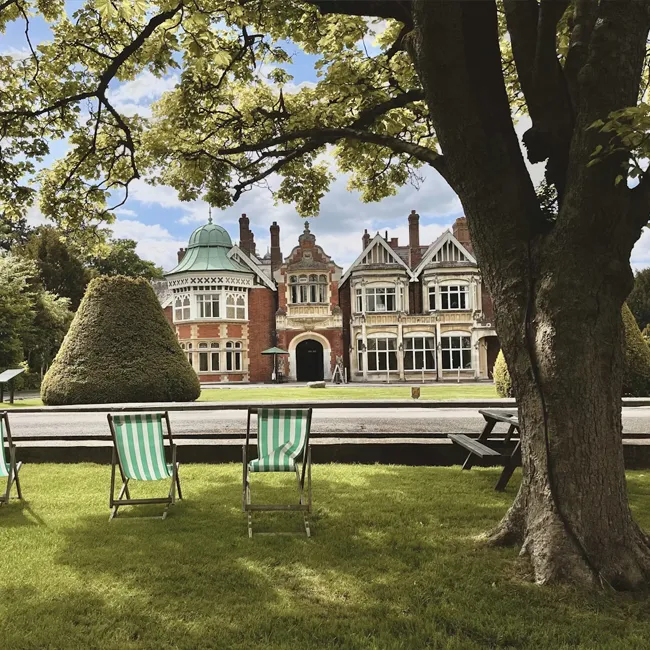 A large redbrick period mansion with ornate gables seen across a lawn with deckchairs and a tree