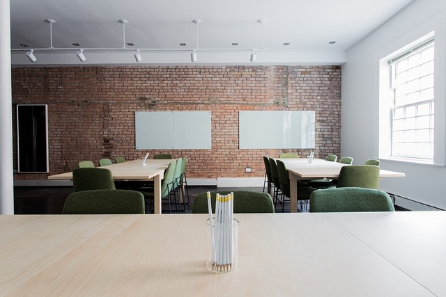 An empty meeting room with a brick wall, two whiteboards, tables and green chairs