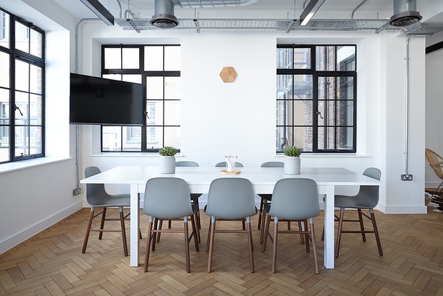 A meeting room with a long white table, grey chairs and a wall-mounted tv