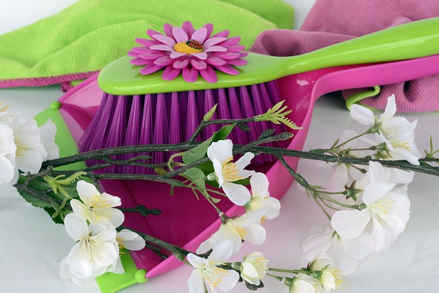A pink dustpan and brush with green and pink cloths, decorated with white flowers