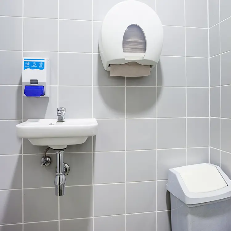 A wall-mounted soap dispenser, paper towel dispenser, sink and bin in a tiled washroom