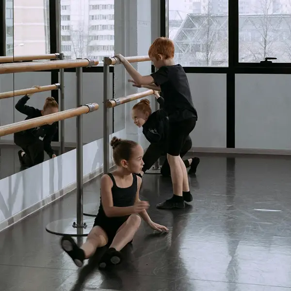 Children at a ballet barre in a dance studio with a mirrored wall and city view through windows