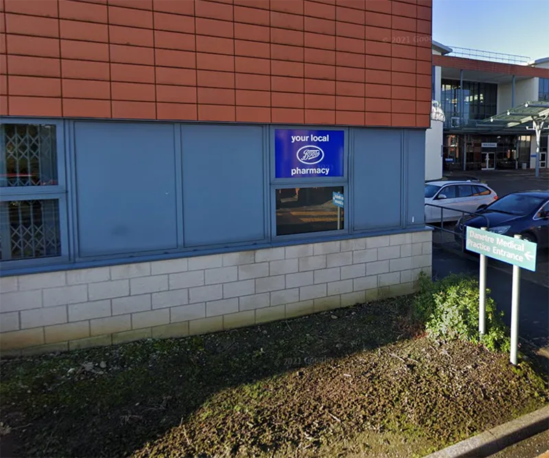 A brick and blue-panelled building with a pharmacy sign and a car park in front