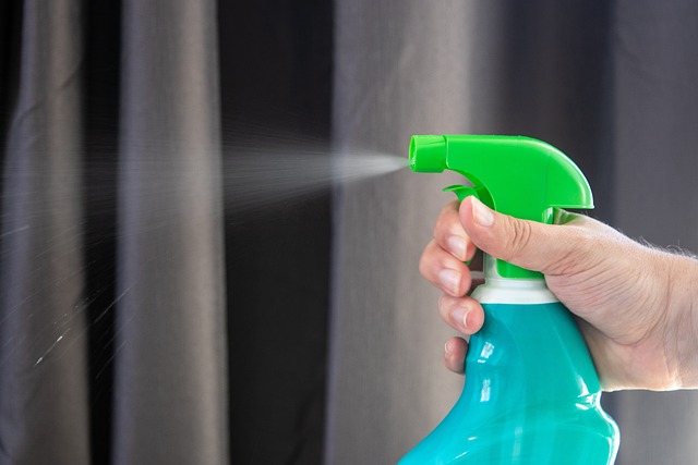 A hand spraying a green and teal trigger spray bottle, with visible mist