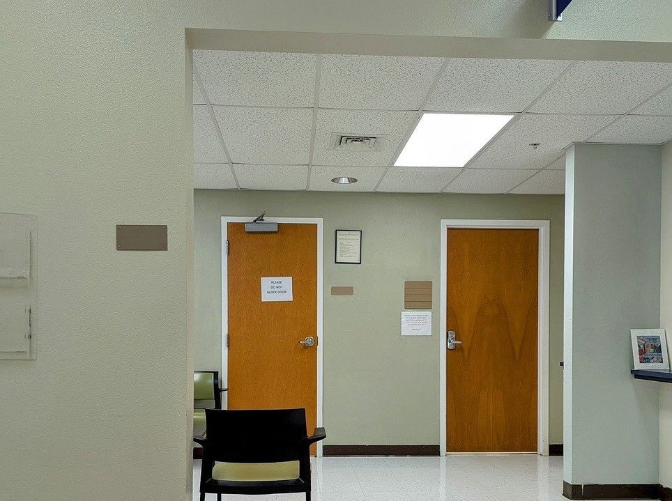 An office corridor with two wood veneer doors, a black chair and a "please do not block door" sign