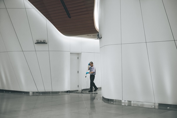 A cleaner mopping a shiny floor in a curved white corridor with a wood-panelled ceiling