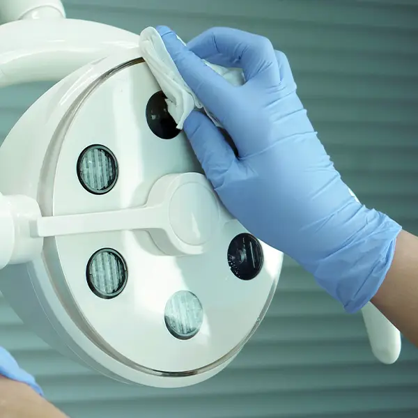 A gloved hand wiping a round light fixture with multiple small mirrored lenses using a cloth
