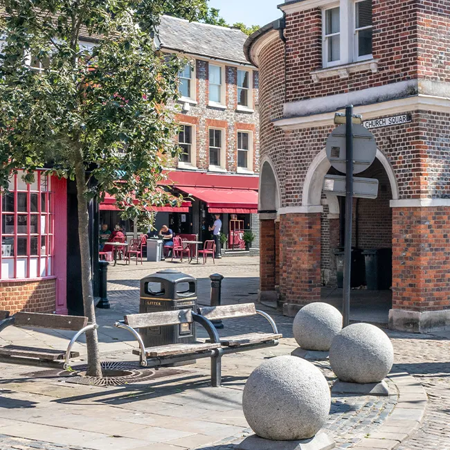 A paved town square with a brick building, benches and stone bollards
