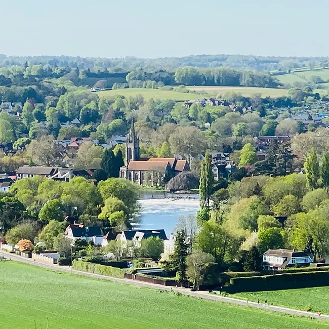 An aerial view of a riverside town with a church spire among trees and rooftops