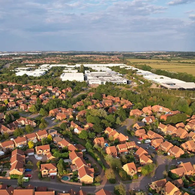 Aerial view of large warehouse buildings next to housing estates and green fields