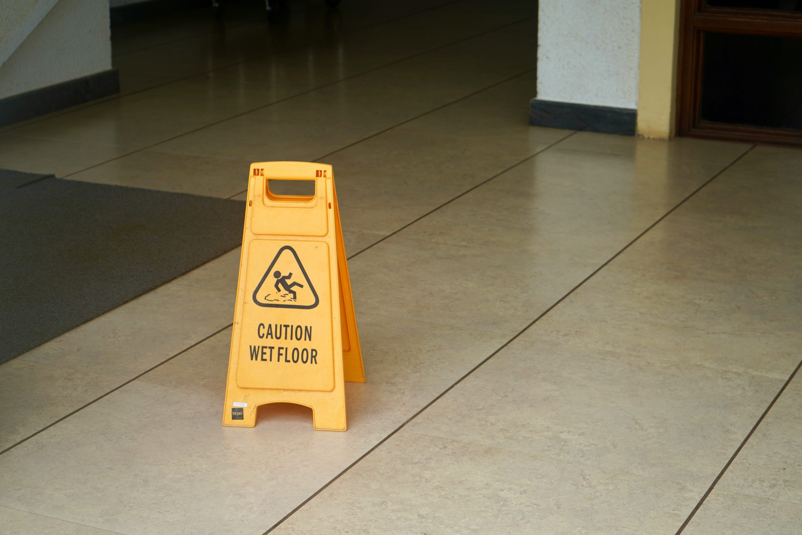 A yellow caution wet floor sign on a tiled floor near an open doorway