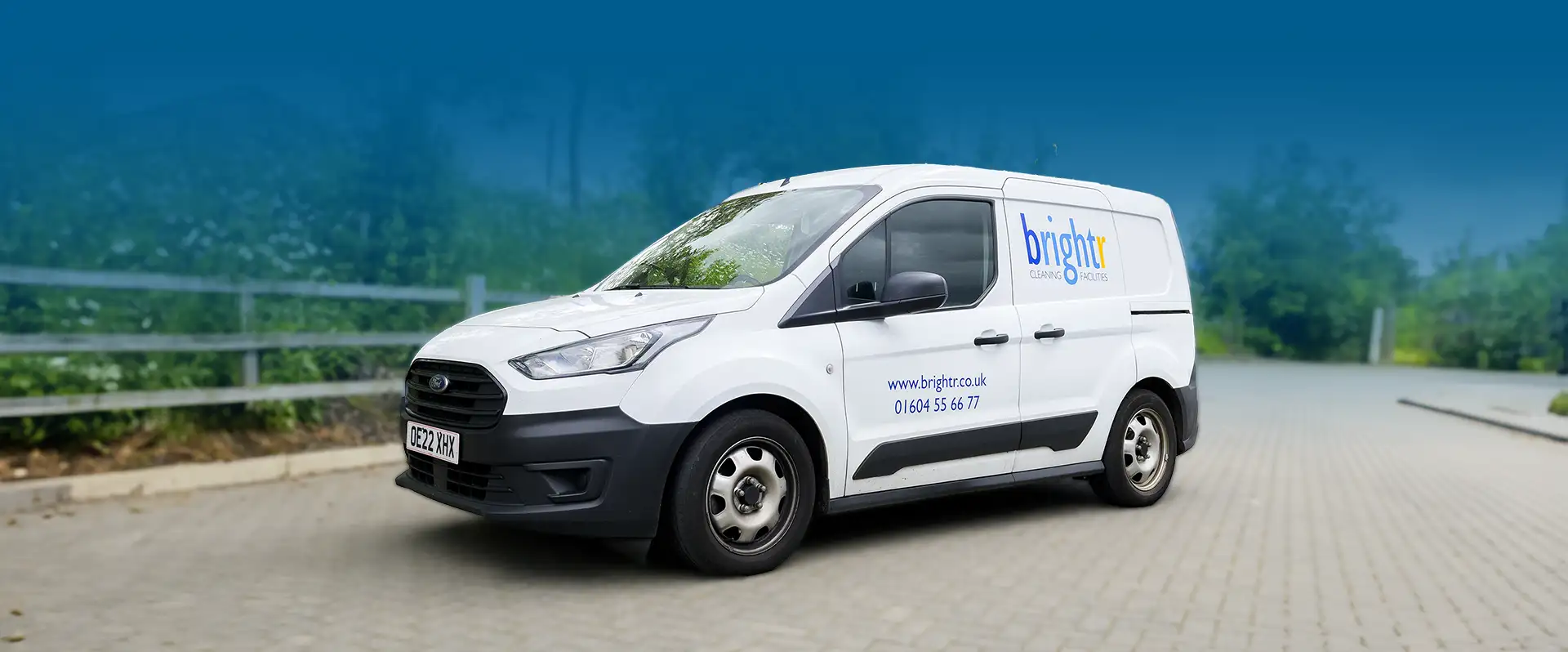 A branded white van parked on a driveway with trees behind, blue tinted background