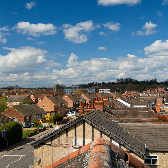 Aerial view of rooftops, chimneys and streets in a residential area under a blue sky