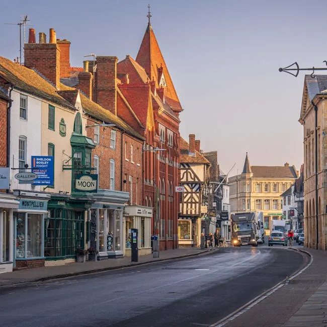 A historic town street at dusk lined with timber-framed buildings, shops and a lorry driving past