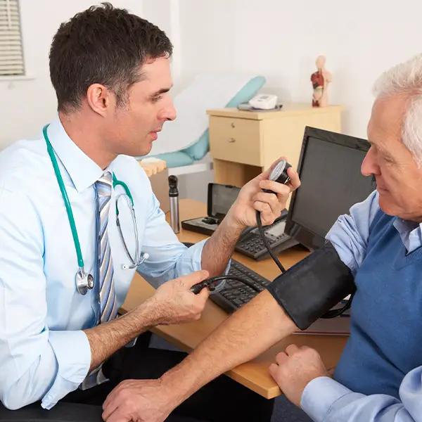 A person with a stethoscope checking an older man's blood pressure in a consulting room